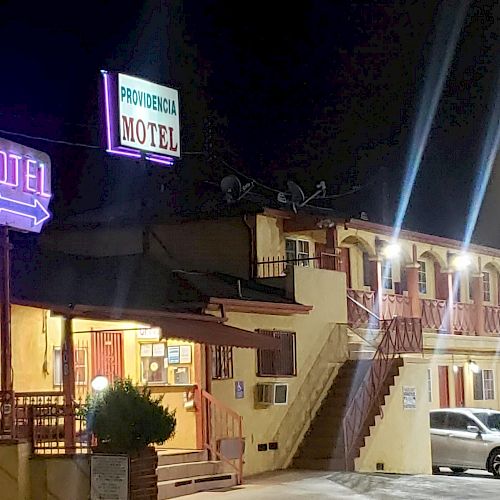 The image shows a two-story motel at night with neon signs that read 