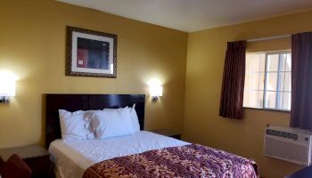 A cozy hotel room with a double bed, bright yellow walls, a framed picture, a window, and a patterned bedspread.