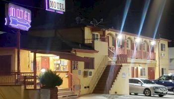 The image shows a two-story motel at night with neon signs and lights; some cars are parked in front, and stairs lead to the second floor.