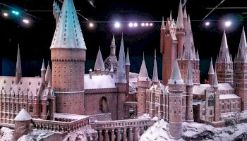 A detailed miniature model of a fantastic castle with tall spires, towers, and snowy surroundings under stage lighting is shown in the image.