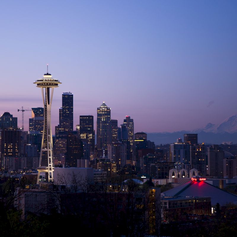The image depicts the Seattle skyline at dusk, featuring the Space Needle prominently, with Mount Rainier visible in the background.