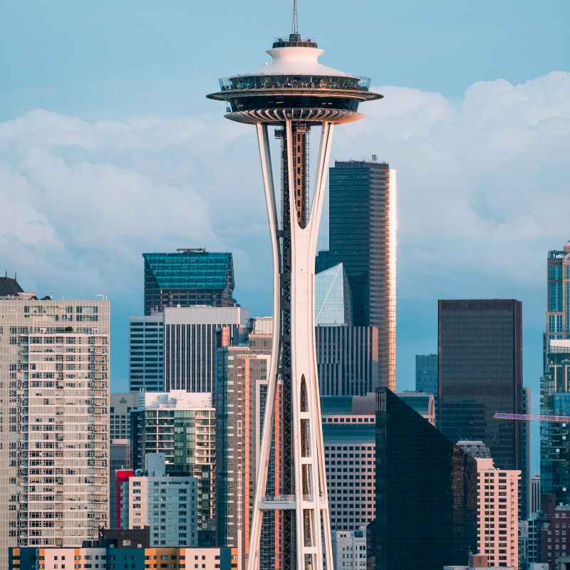 The image shows the Space Needle against a backdrop of modern skyscrapers and buildings in Seattle, Washington.