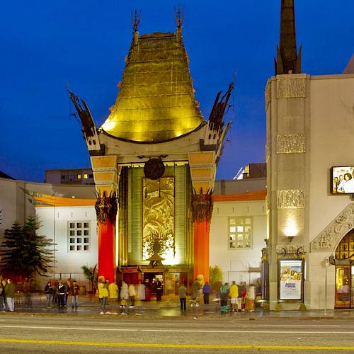 The image depicts the front view of a famous theater with a distinct architectural design, lit up at night with people gathered outside.