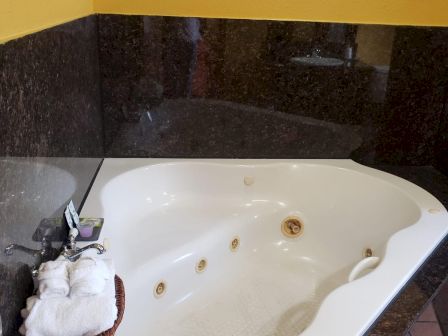 The image shows a corner bathtub with a few jets, towels in a basket, and some toiletries on the edge, set against a tiled wall.