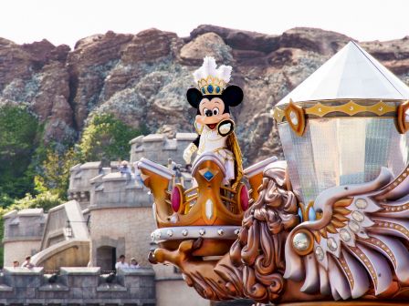 The image shows a float with a character dressed as a king, on a fairytale-themed backdrop, likely at a theme park.